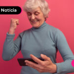 Imagem mostra pessoa de idade segurando um celular e comemorando algo.