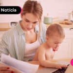 Pessoa segurando um bebê e um papel em frente ao computador