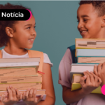 Duas crianças segurando uma pilha de livros cada uma e se olhando enquanto sorriem.