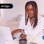Pessoa anotando em um caderno e mexendo no computador