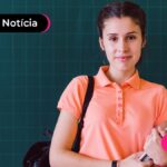 Jovem sorrindo segurando cadernos e com mochila nas costas.