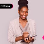Jovem sorrindo segurando caderno e caneta.