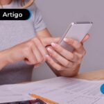 Papéis espalhados pela mesa e pessoa mexendo no celular.