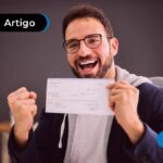 Jovem sorrindo e comemorando segurando um cheque.
