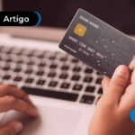 Duas mãos, uma elas está em um notebook e a outra segurando um cartão.