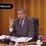 Pessoa de mais idade usando terno cinza escuro falando em reunião.