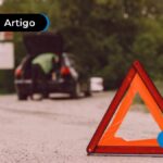 Triângulo vermelho de sinalização no meio da rua e carro parado no fundo.