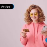 Pessoa sorrindo segurando um cartão e um celular