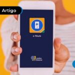Pessoa segurando celular com aplicativo do E-Título na tela.