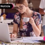 Jovem segurando xícara de café e mexendo em notebook.