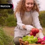 Pessoa jovem sorrindo colhendo legumes em horta.