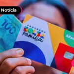 Pessoa segurando cartão do bolsa família e nota de cem reais.