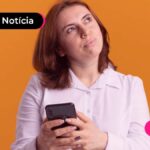 Jovem com expressão de dúvida olhando para cima e segurando um celular. No fundo, uma parede laranja.