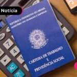 calculadora preta, caneta e carteira de trabalho em mesa de madeira.