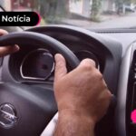 Motorista de aplicativo com as mãos no volante de carro.