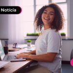 Jovem sorrindo enquanto usa computador para trabalhar.