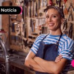 Mulher em uma oficina com uma blusa azul e com uma bandana no seu cabelo raspado e uma bicicleta ao lado esquerdo dela