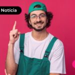 homem com um boné verde para trás, com uma blusa branca e usando óculos