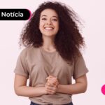 Moça com camisa bege sorrindo com cabelo cacheado grande