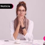 mulher de blusa branca com um cachecol marrom com cabelo amarrado em um coque usando óculos