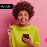 Jovem sorrindo enquanto usa celular pra ler notícia sobre consignado CLT direto com os bancos.
