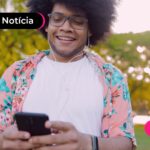 Jovem sorrindo enquanto usa celular para fazer consignado privado.