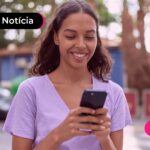 Pessoa de blusa lilás segurando o celular enquanto está sorrindo.
