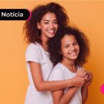 Pessoa de blusa branca abraçando criança de blusa branca, enquanto estão sorrindo.