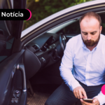 Pessoa sentada no banco do motorista de carro olhando para celular.