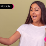 Pessoa de blusa branca segurando celular e comemorando.