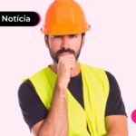 Pessoa com capacete na cabeça, blusa preta e colete amarelo com a mão no queixo com expressão pensativa.