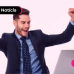 Pessoa de terno olhando para computador com os dois braços levantados e expressão feliz.