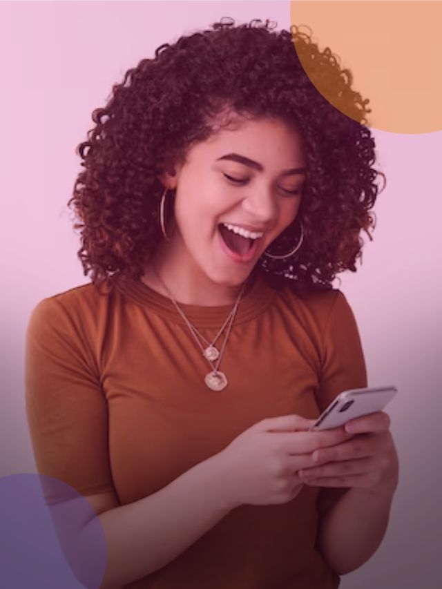 Mulher jovem sorrindo enquanto olha para o celular, animado com uma boa oferta de crédito.