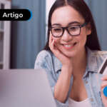 Mulher sorri ao usar notebook e segura cartão, representando compras ou transações online.