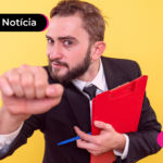 Pessoa de terno com punho fechado segurando prancheta vermelha.