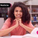 Pessoa de blusa rosa estudando em biblioteca.