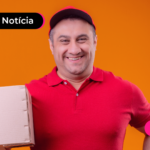 Pessoa de blusa vermelha e chapéu segurando uma caixa enquanto está sorrindo.