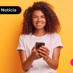 Pessoa de blusa branca sorrindo enquanto segura celular.