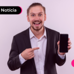 Pessoa de camisa social e blazer preto com expressão alegre apontando para celular.