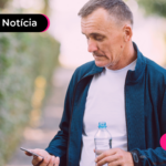 Pessoa idosa de blusa branca e casaco azul olhando para celular com expressão triste.