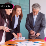 Pessoas de terno olhando tablet ao redor de uma mesa.