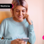 Pessoa de blusa azul segurando celular e sorrindo.