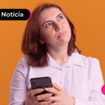 Pessoa de blusa branca segurando celular com expressão de dúvida.