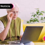 Pessoa idosa olhando para notebook enquanto está sentada em sofá.