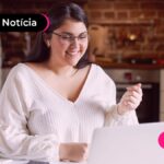Jovem mulher sorrindo lendo no computador sobre notícia de migração de consignado CLT para novo modelo.