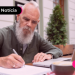 Pessoa idosa olhando para agenda enquanto está com o notebook aberto.