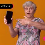 Idosa apontando para o celular com expressão surpresa ao saber de aviso do INSS a aposentados com direito a ressarcimento.