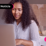 Jovem sorrindo enquanto usa computador para ler notícia sobre Programa Reforma Brasil.