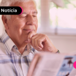 Pessoa idosa olhando para jornal com expressão feliz.