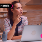 Mulher em escritório com mão no queixo e expressão pensativa.